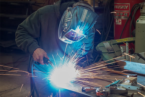 As his MIG welder whirrs, a masked Mazurowski is enveloped in a halo of sparks