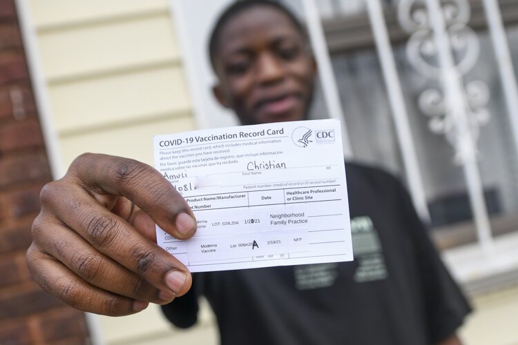Medical assistant Christian Amuli, of Neighborhood Family Practice, holds up a copy of his vaccination card.