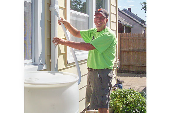Dave Kasik, BPDC Senior Services Coordinator helps install an Oatey Mystic downspout diverter for the rain barrel
