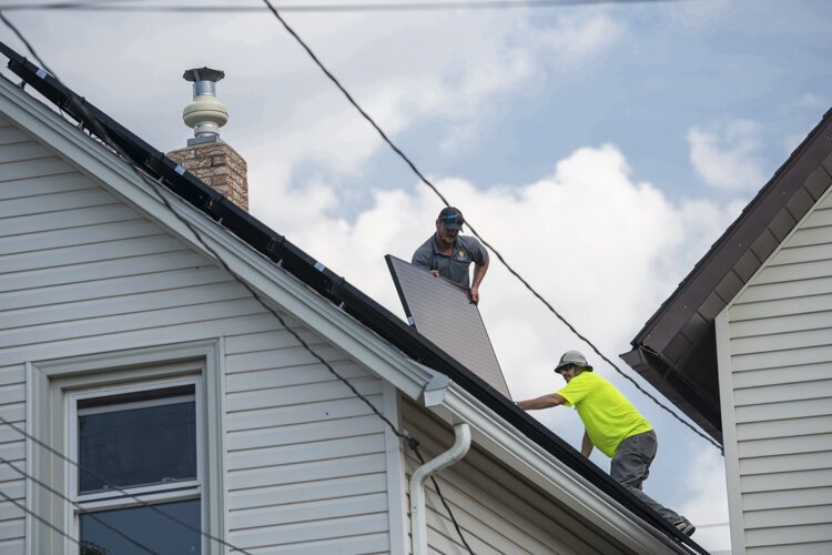 Workers install solar panels to the roof of a residential home.