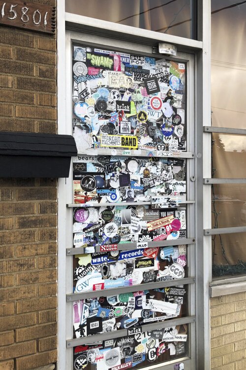 The front door of the former Music Saves record store is plastered with band decals.