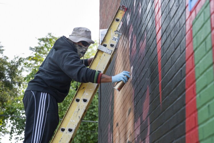 Artist Osman Swimr Muhammad working on his temporary mural on a slated for demolition building on W25th Street.
