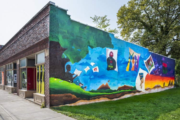 Storytime (BLM)” depicts a young Black boy under a tree, reading a story about his ethnicity and his family. The artists are Lacy “Lacerrrr” Talley, Michelle Suells, Aldonte Flonnoy, and Niquo Braxton.